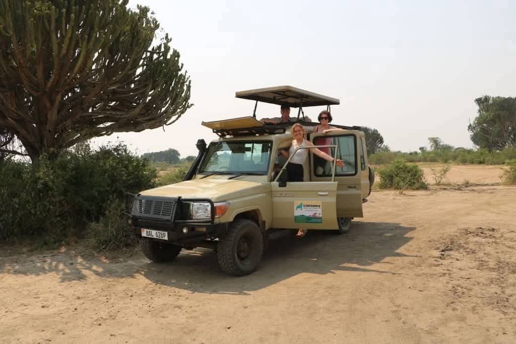 A Confidence Africa Tours Land Cruiser with its pop-up roof raised beside a candelabra euphorbia on dry savannah
