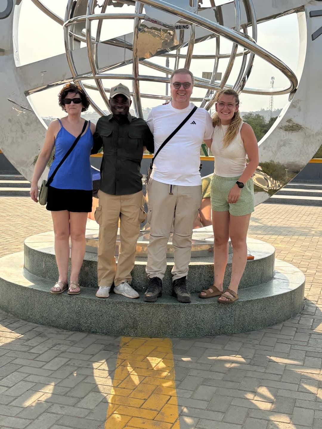 Des voyageurs et leur guide sous le globe du monument de l’Équateur en Ouganda
